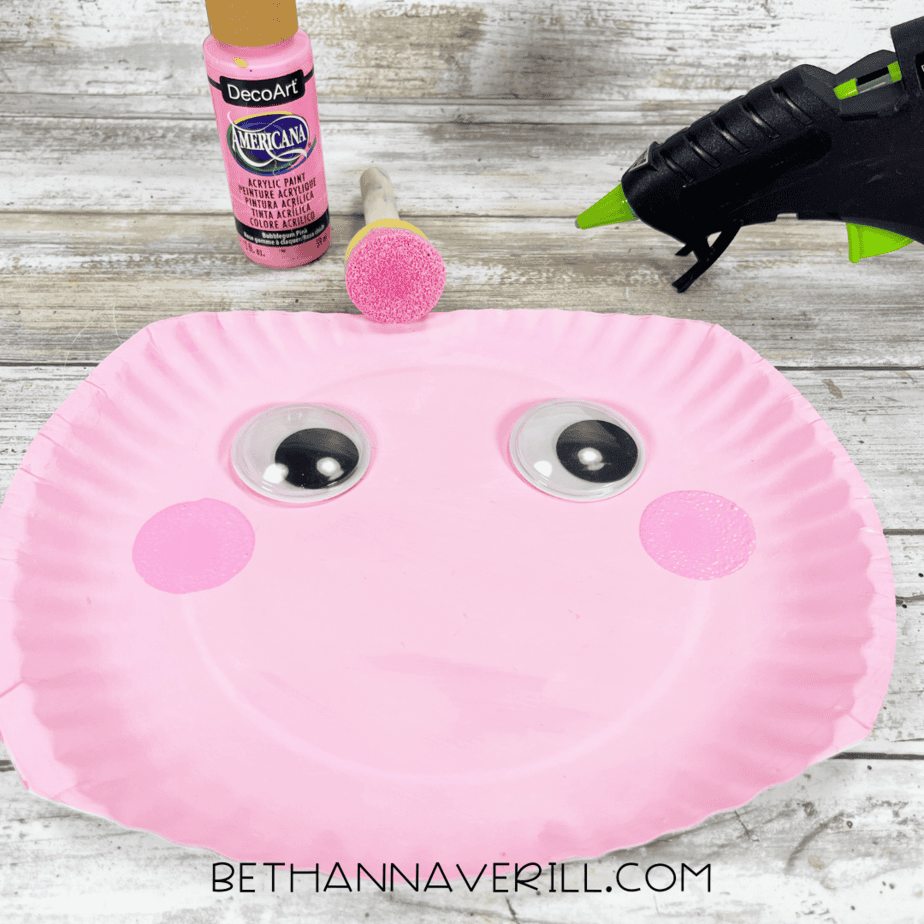 Paper plate with googly eyes and painted rosy cheeks.