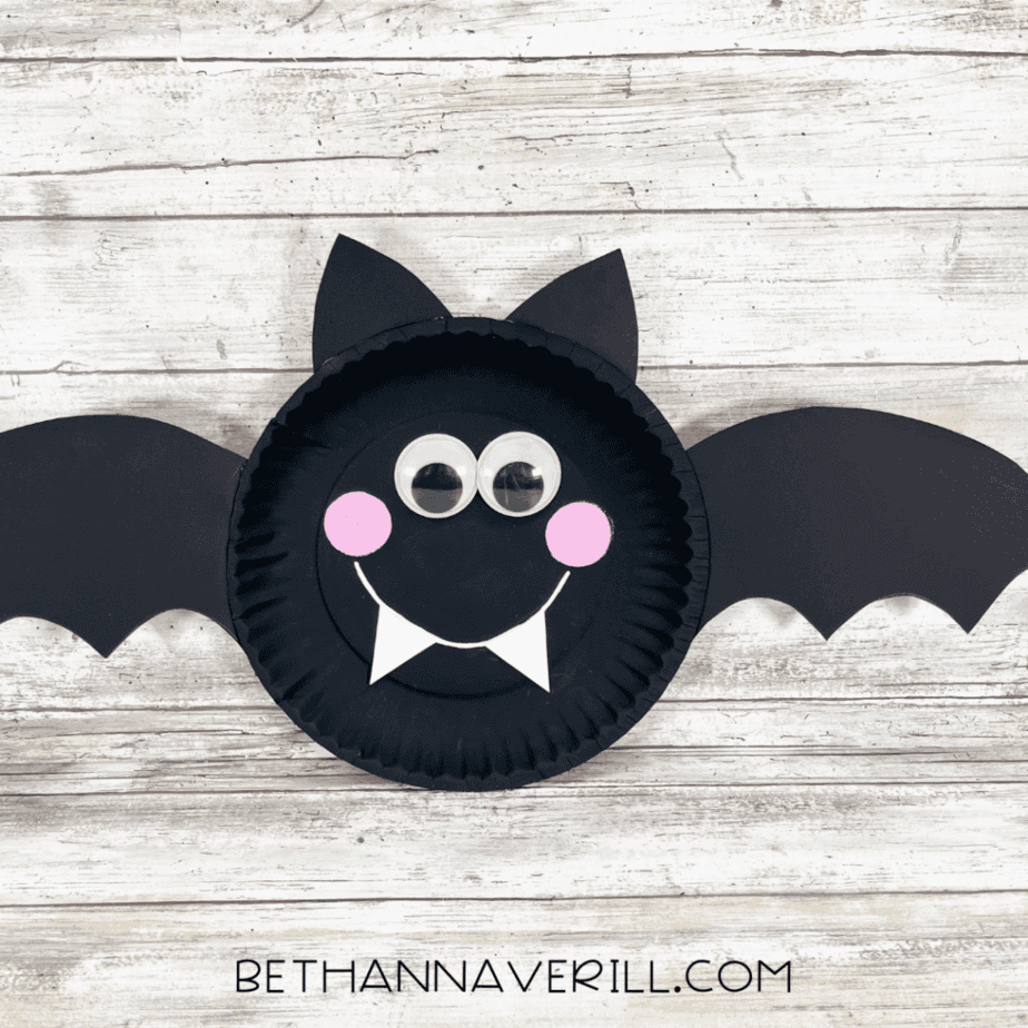 Finished bat paper plate craft with black wings, pointy ears, googly eyes, pink cheeks, and white fangs.