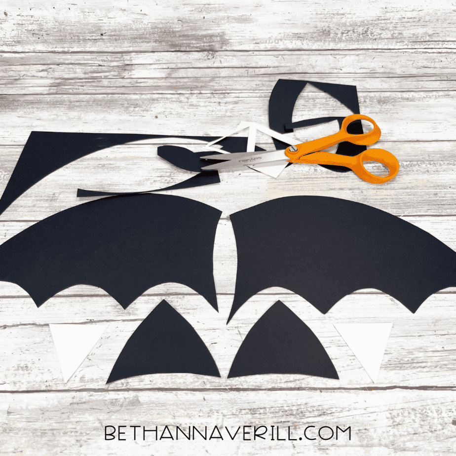 Cut out bat wings and ears from black paper laid out with scissors.