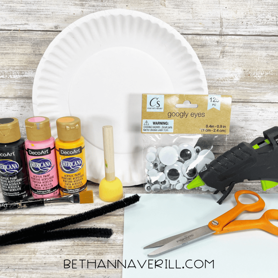Craft materials including paints, googly eyes, pipe cleaners, scissors, glue gun, and a paper plate.