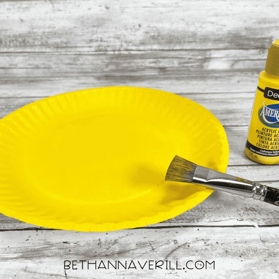 Paper plate painted bright yellow with a paintbrush and yellow paint nearby.