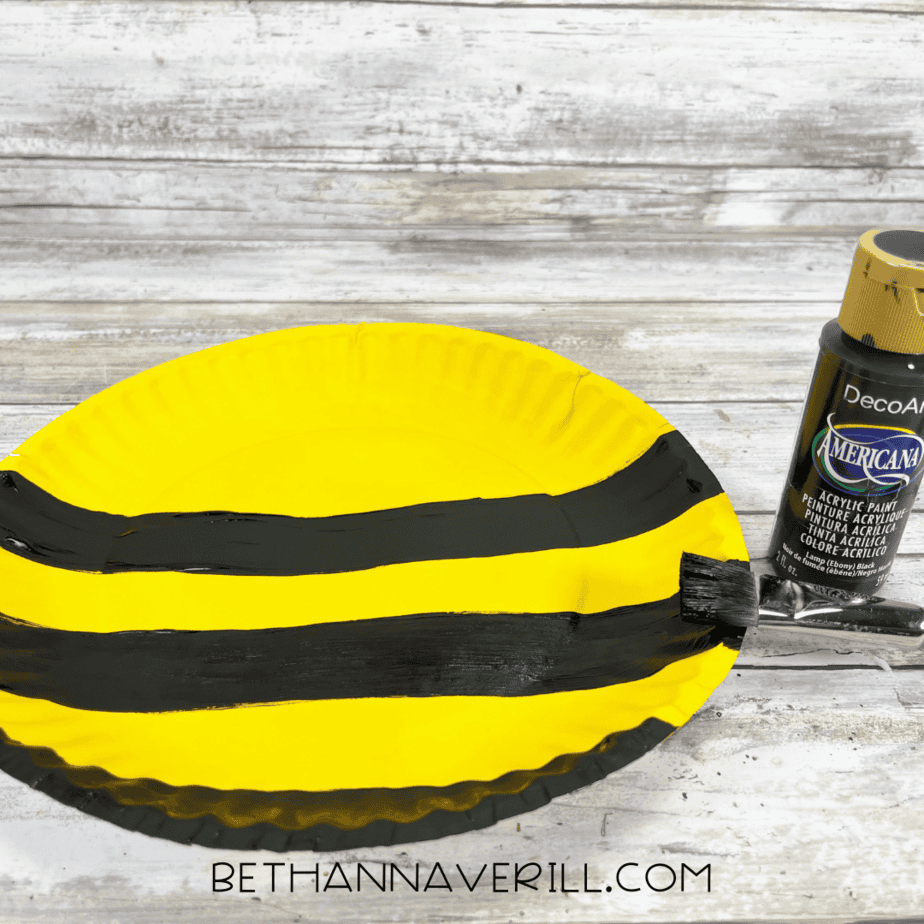 Yellow paper plate with thick black stripes painted across it.