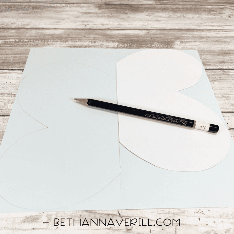 Pencil tracing large wing shapes on light blue paper.