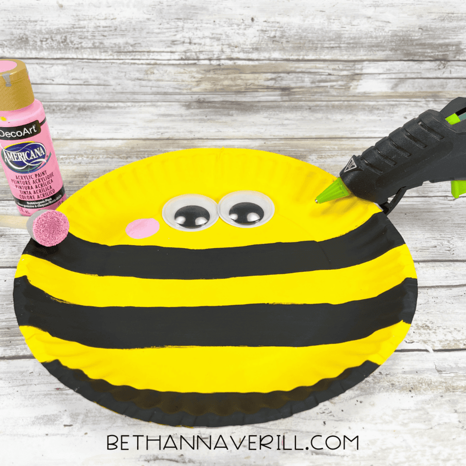 Yellow plate with googly eyes and pink cheeks being glued in place.