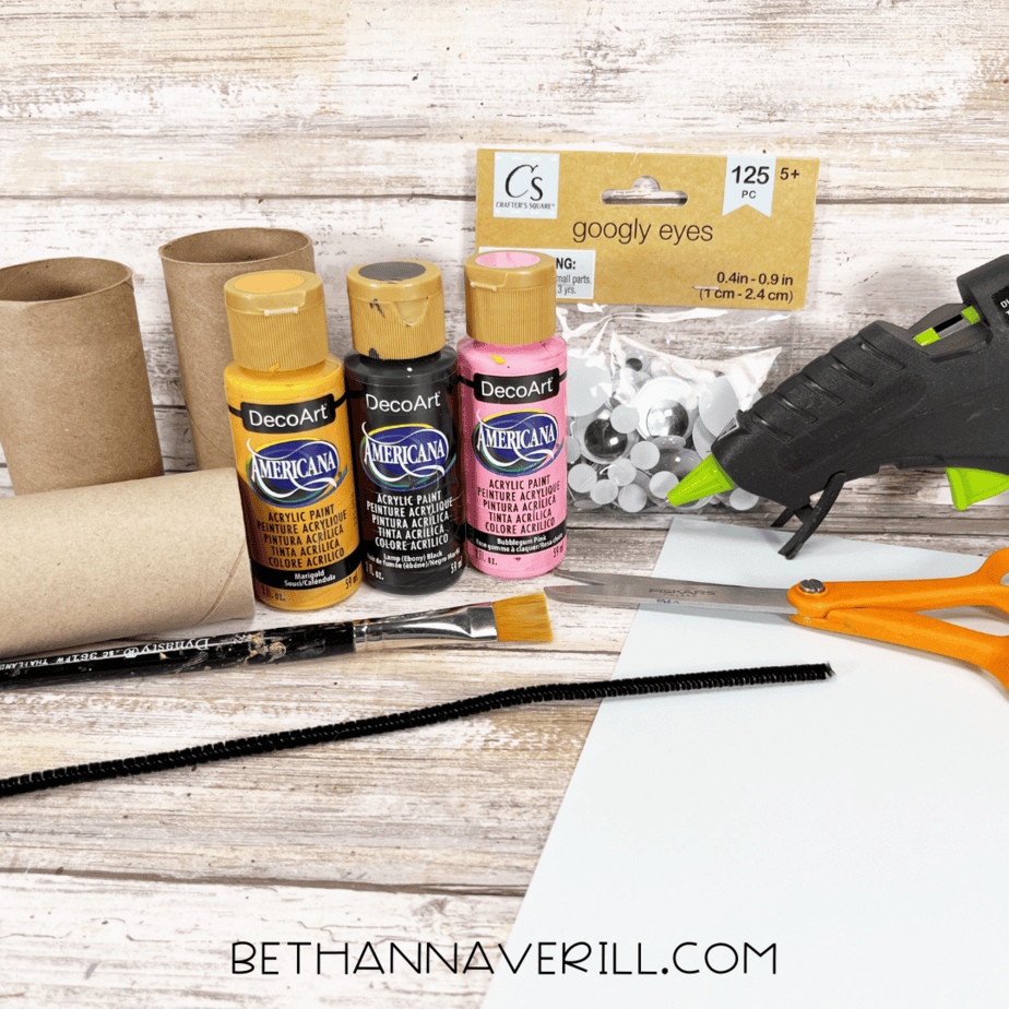 Toilet paper roll craft supplies laid out, including paint, googly eyes, paper, and glue gun.