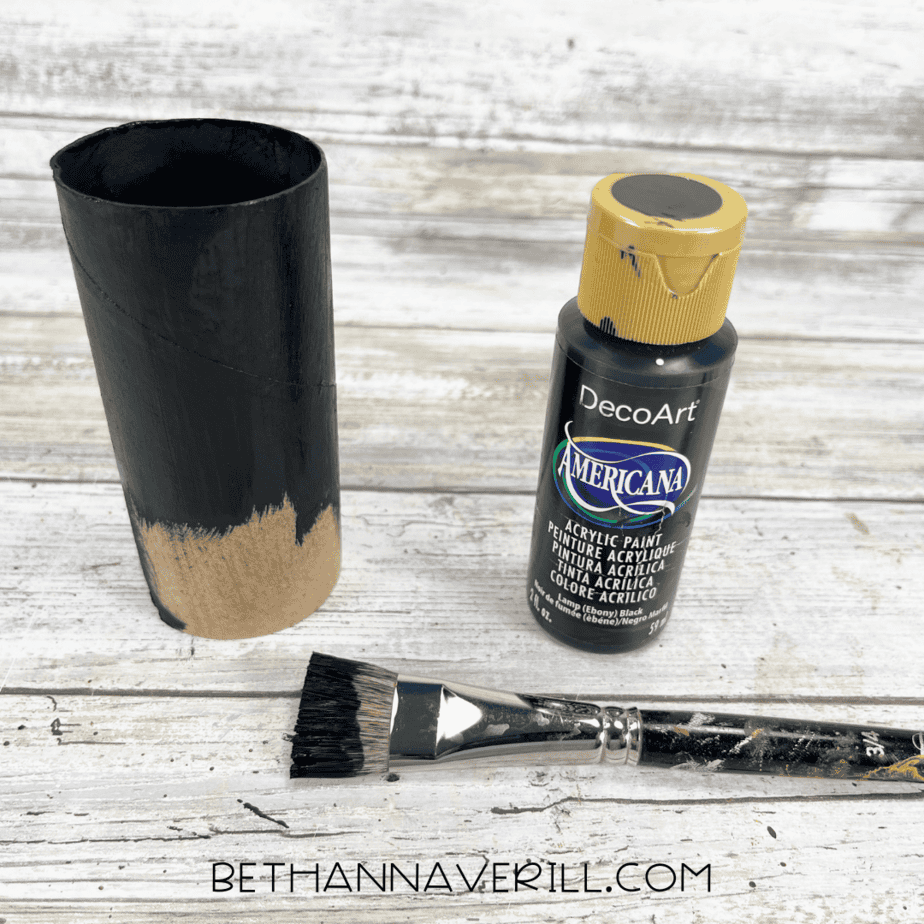 Toilet paper roll being painted black with a paintbrush.