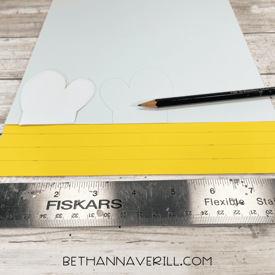 White and yellow paper with bee wings and stripe templates drawn on, pencil and ruler nearby.