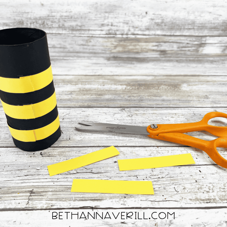 excess paper being trimmed off bee body with yellow stripes glued on, scissors nearby.