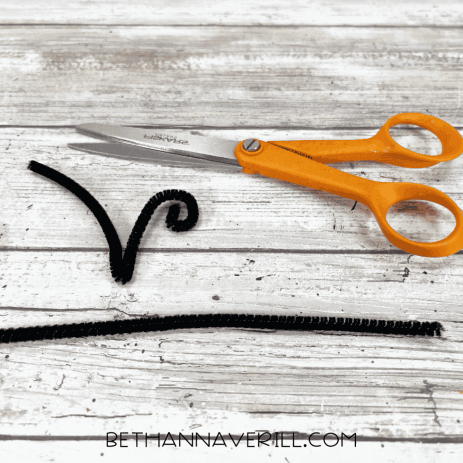 Black pipe cleaner cut and curled into bee antennae next to scissors.