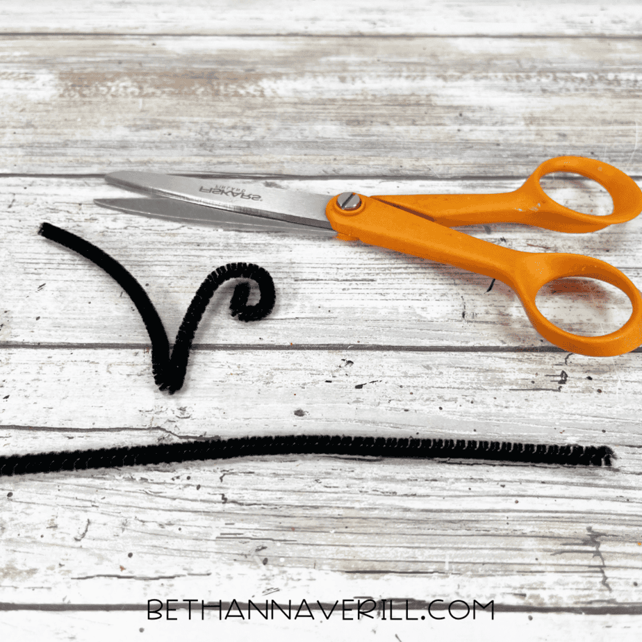Black pipe cleaner cut and curled into bee antennae next to scissors.