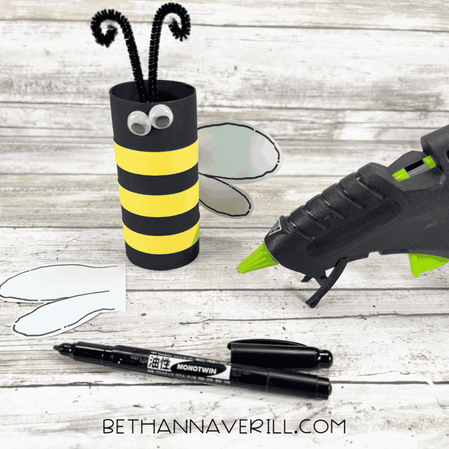 Bee paper roll with antennae, wings, and googly eyes being glued in place.