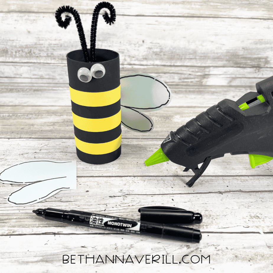 Bee paper roll with antennae, wings, and googly eyes being glued in place.