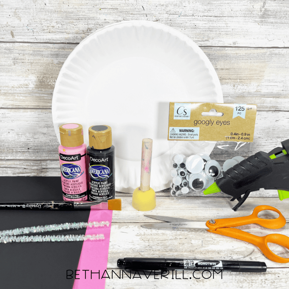 Craft supplies for black cat paper plate craft, including paint, googly eyes, paper, pipe cleaners, and scissors.