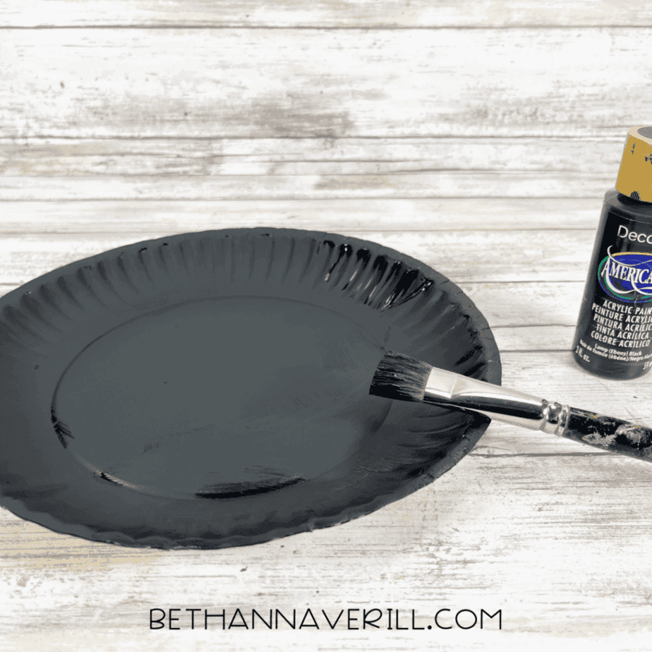 Paper plate painted black with brush and black paint bottle.