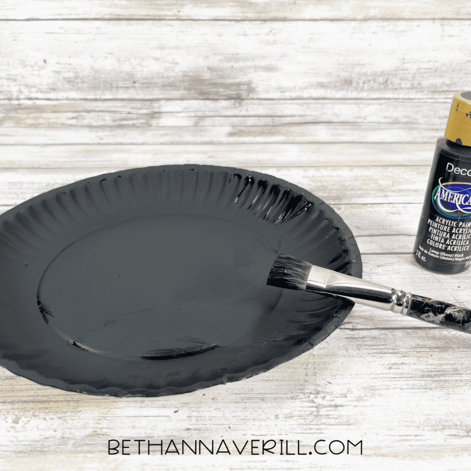 Paper plate painted black with brush and black paint bottle.