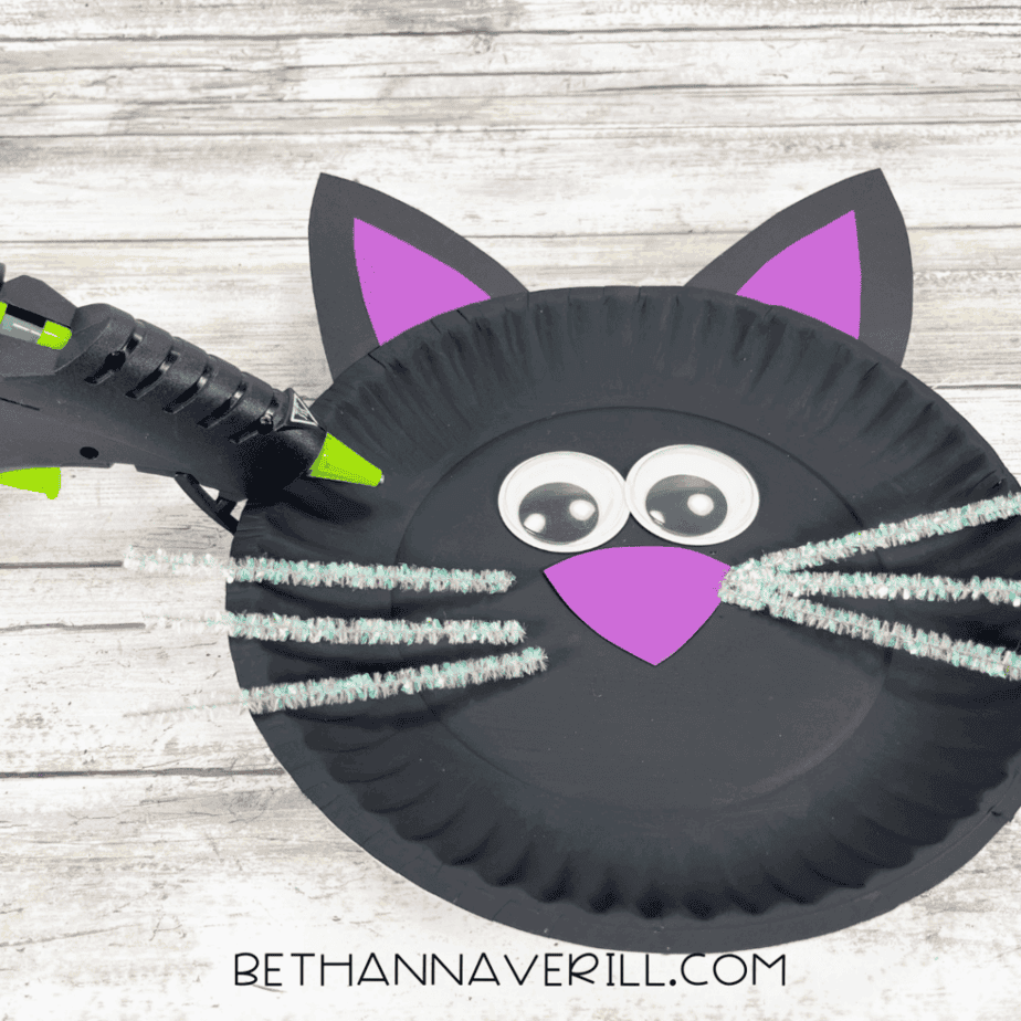Black cat paper plate with whiskers being glued onto the face.