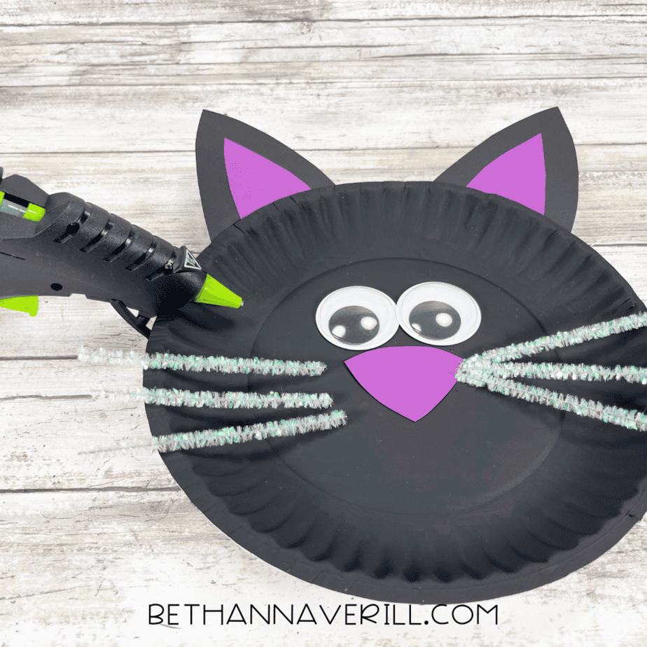 Black cat paper plate with whiskers being glued onto the face.