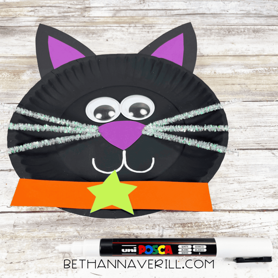 Black cat paper plate with googly eyes, purple nose, whiskers, and orange collar with green star.