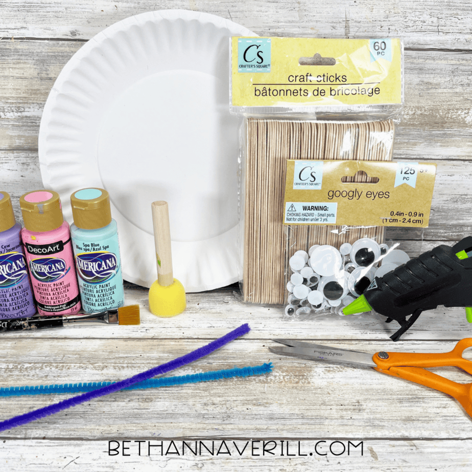Craft supplies laid out for butterfly paper plate craft including paint, googly eyes, sticks, and pipe cleaners.