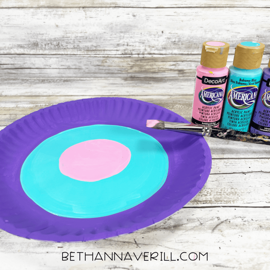 Paper plate painted purple, blue, and pink in concentric rings.