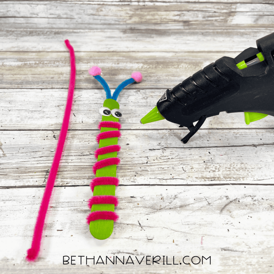 Green craft stick wrapped with a pink pipe cleaner and googly eyes glued on.