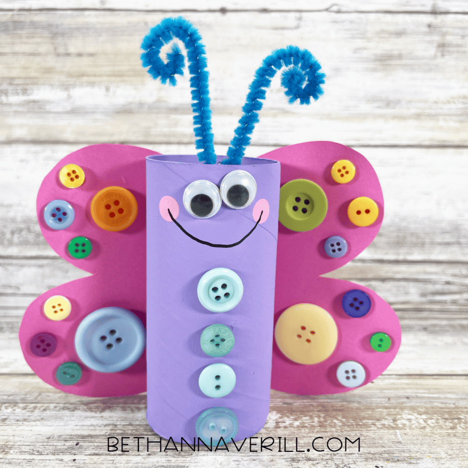 Completed butterfly paper roll craft with pink button wings, blue antennae, and smiling face.