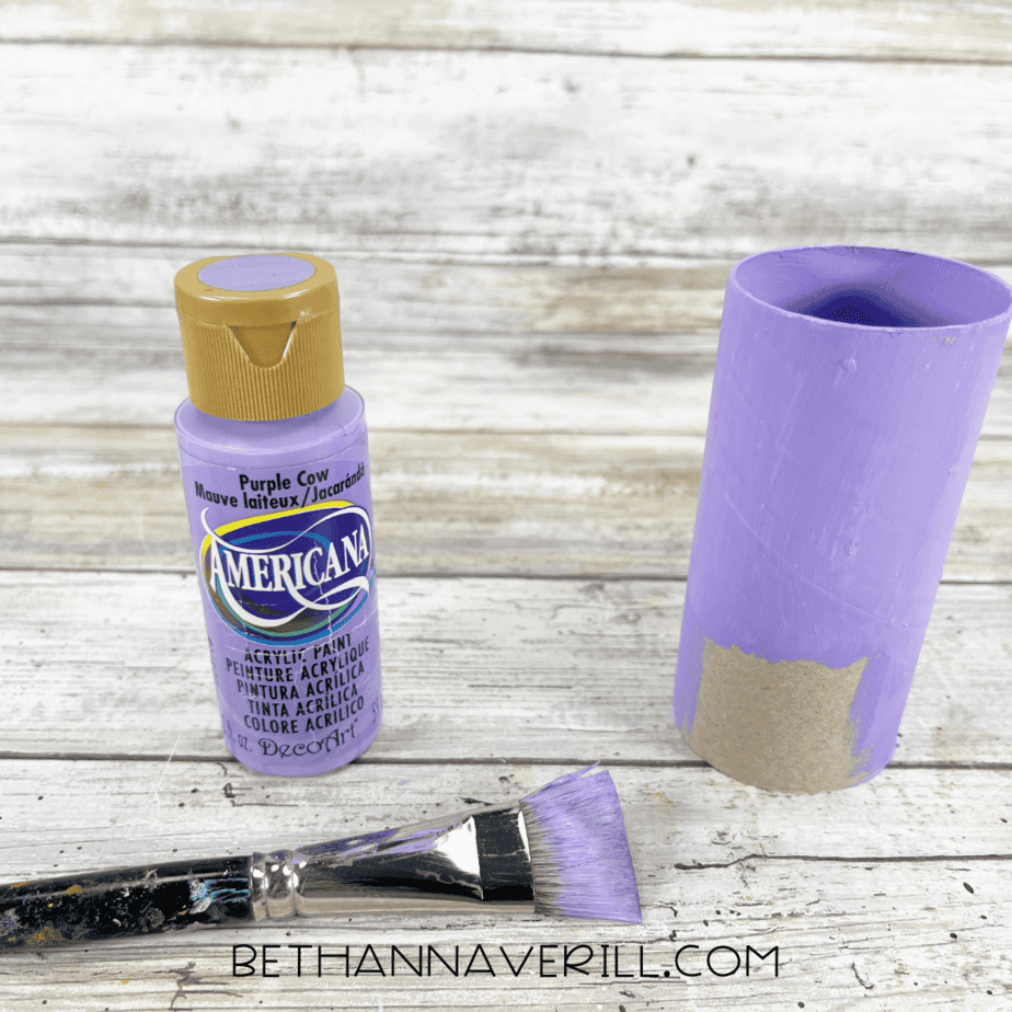 Toilet paper roll painted purple with paint bottle and brush beside it.