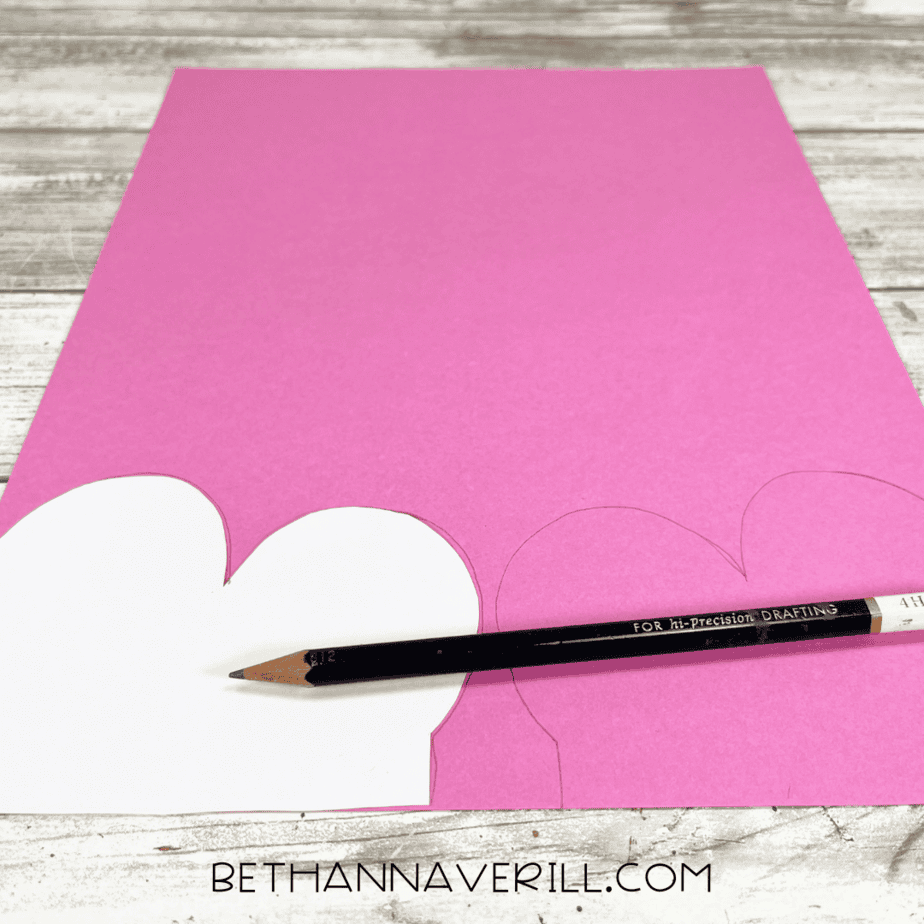 Pink construction paper with wing shapes being traced using a pencil and template.