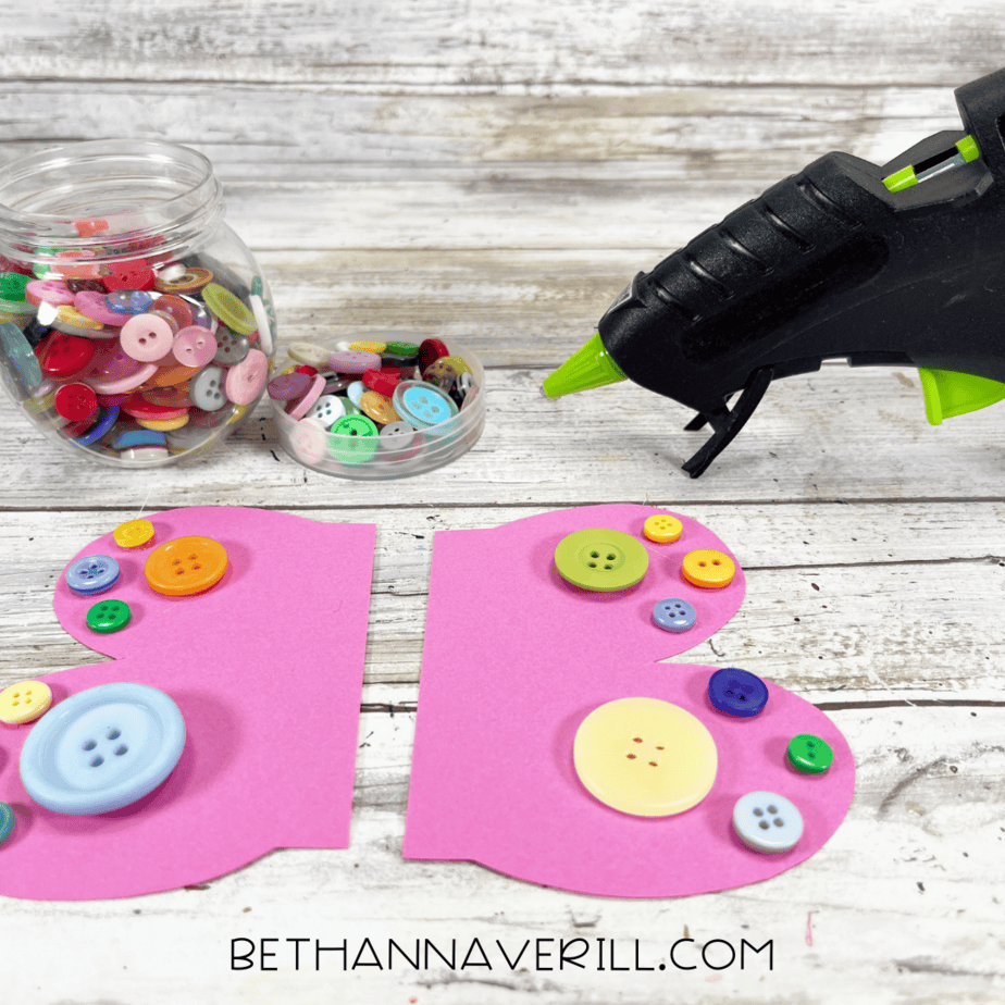 Buttons being glued onto the pink paper wings.
