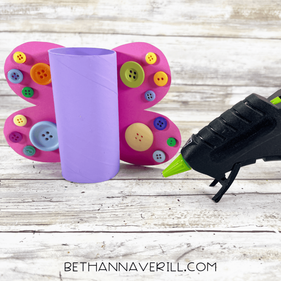 Purple painted toilet paper roll with decorated button wings glued to the back.