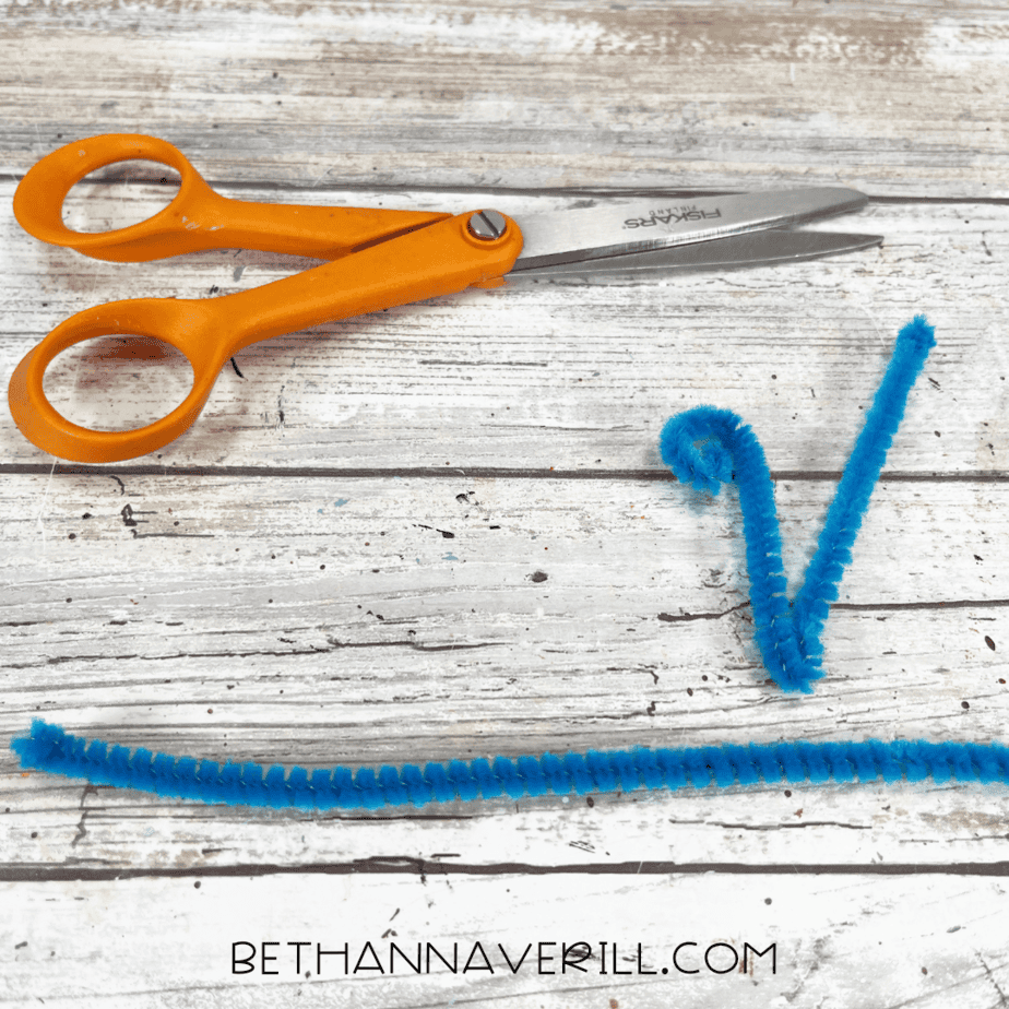 Blue pipe cleaner cut and bent into antenna shapes with scissors beside it.
