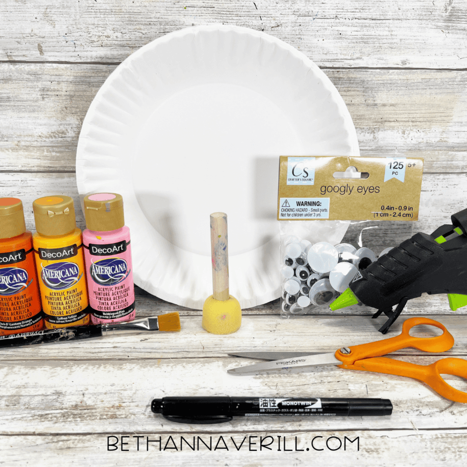 Candy corn craft materials with paint, paper plate, googly eyes, ribbon, glue, and scissors.