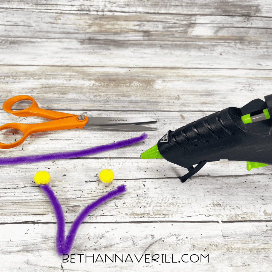 Purple pipe cleaners with yellow pom poms prepared for antennae.