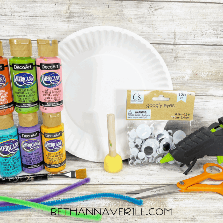 Materials for paper plate caterpillar craft including paints, googly eyes, pipe cleaners, glue, and scissors.