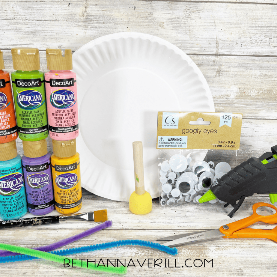 Materials for paper plate caterpillar craft including paints, googly eyes, pipe cleaners, glue, and scissors.
