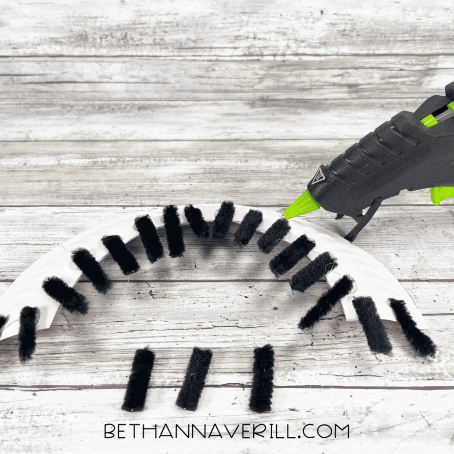 Black pipe cleaners glued along the painted paper plate edge as caterpillar legs.