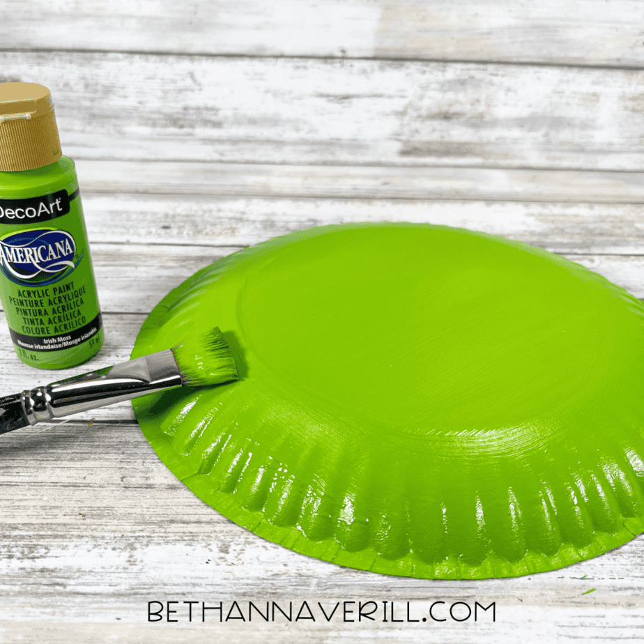 Paper plate painted bright green with a paintbrush and green paint bottle nearby.