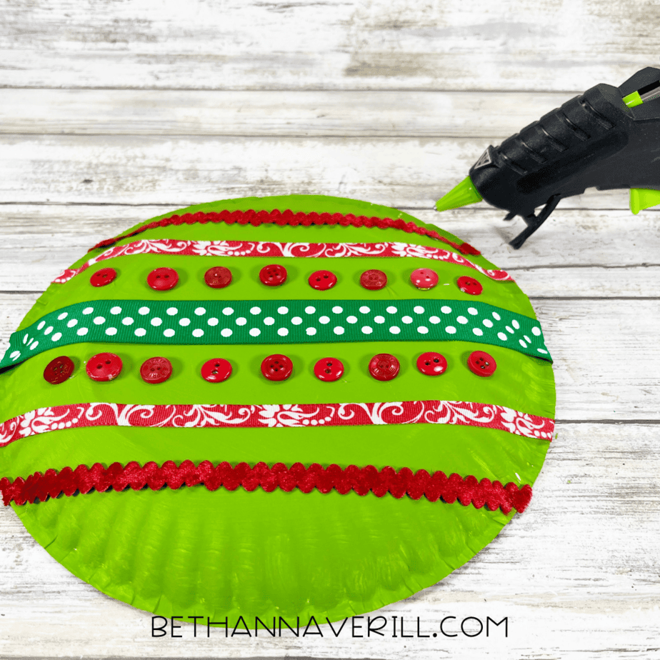 Paper plate decorated with multiple ribbons and buttons in Christmas colors.