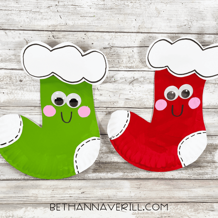 Two finished paper plate Christmas stockings, one red and one green, smiling side by side.