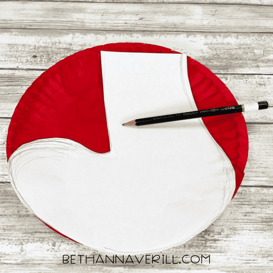Stocking shape template traced on top of the painted red paper plate with pencil.
