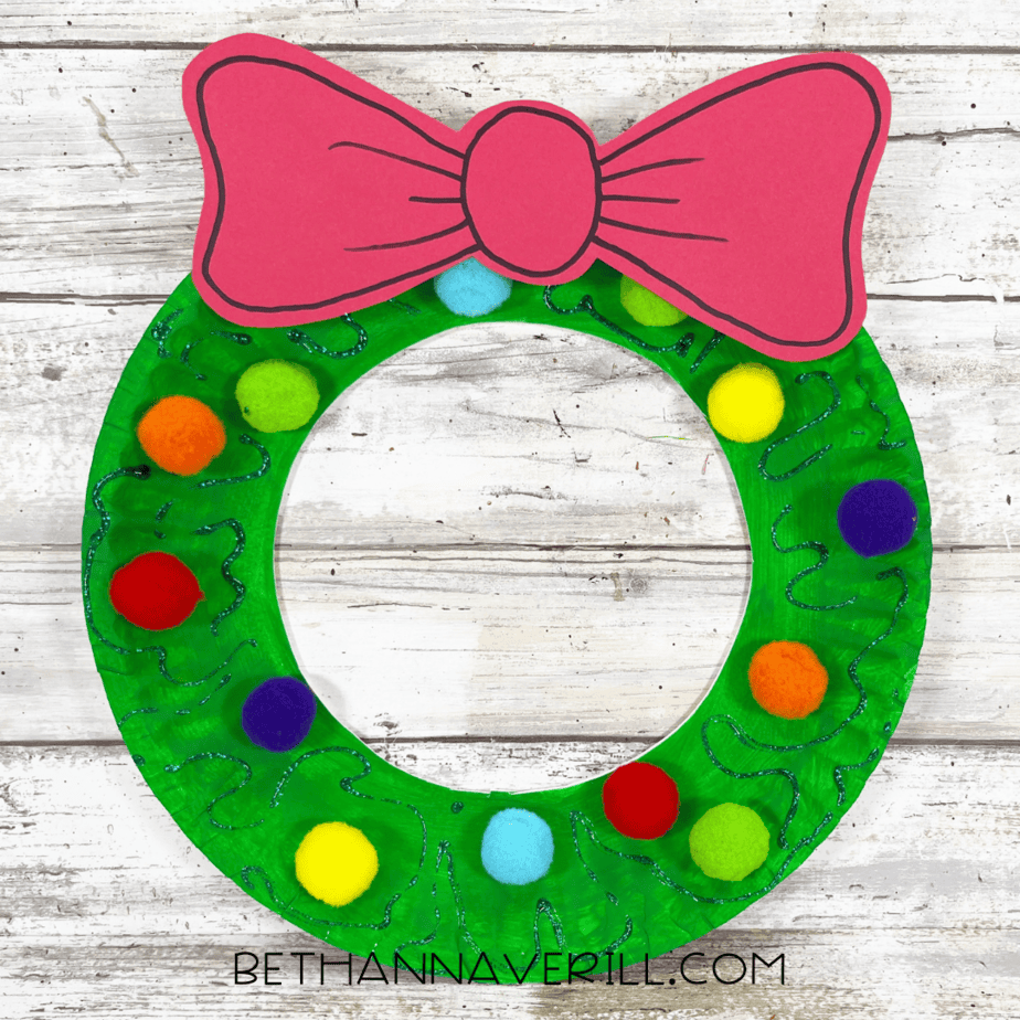 Finished paper plate wreath decorated with pom poms, bow, and glitter glue.