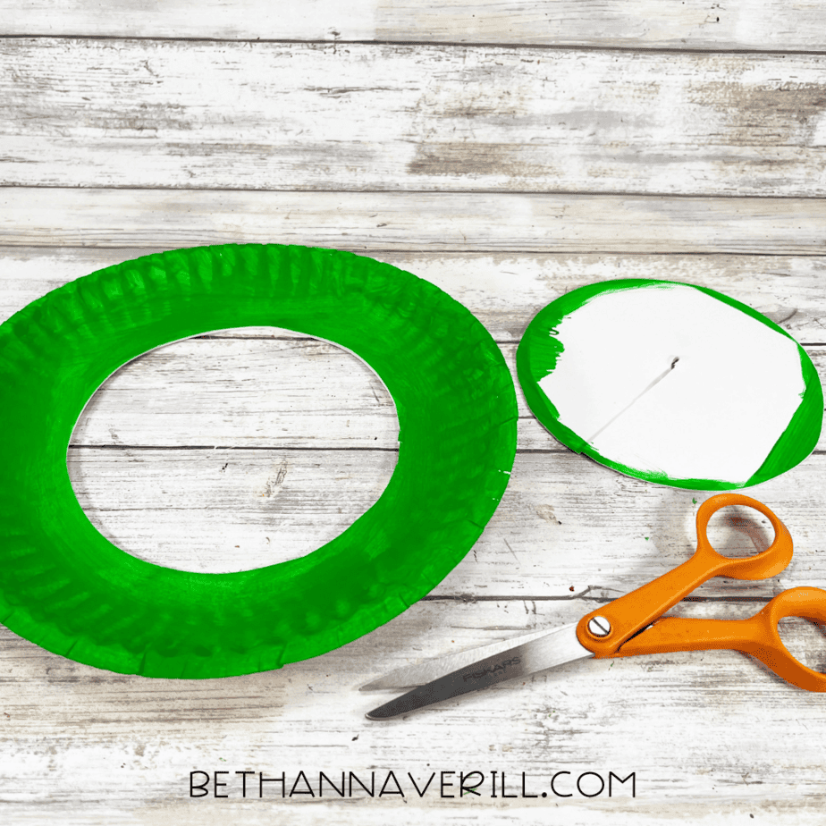 Paper plate with center cut out to form a wreath shape, scissors nearby.