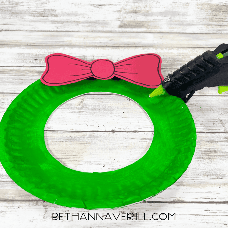 Green paper plate wreath with red bow being glued to the top.