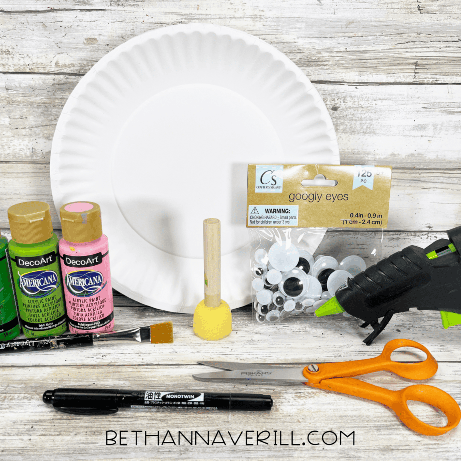 Craft supplies including paints, googly eyes, paper plate, scissors, glue gun, and marker.