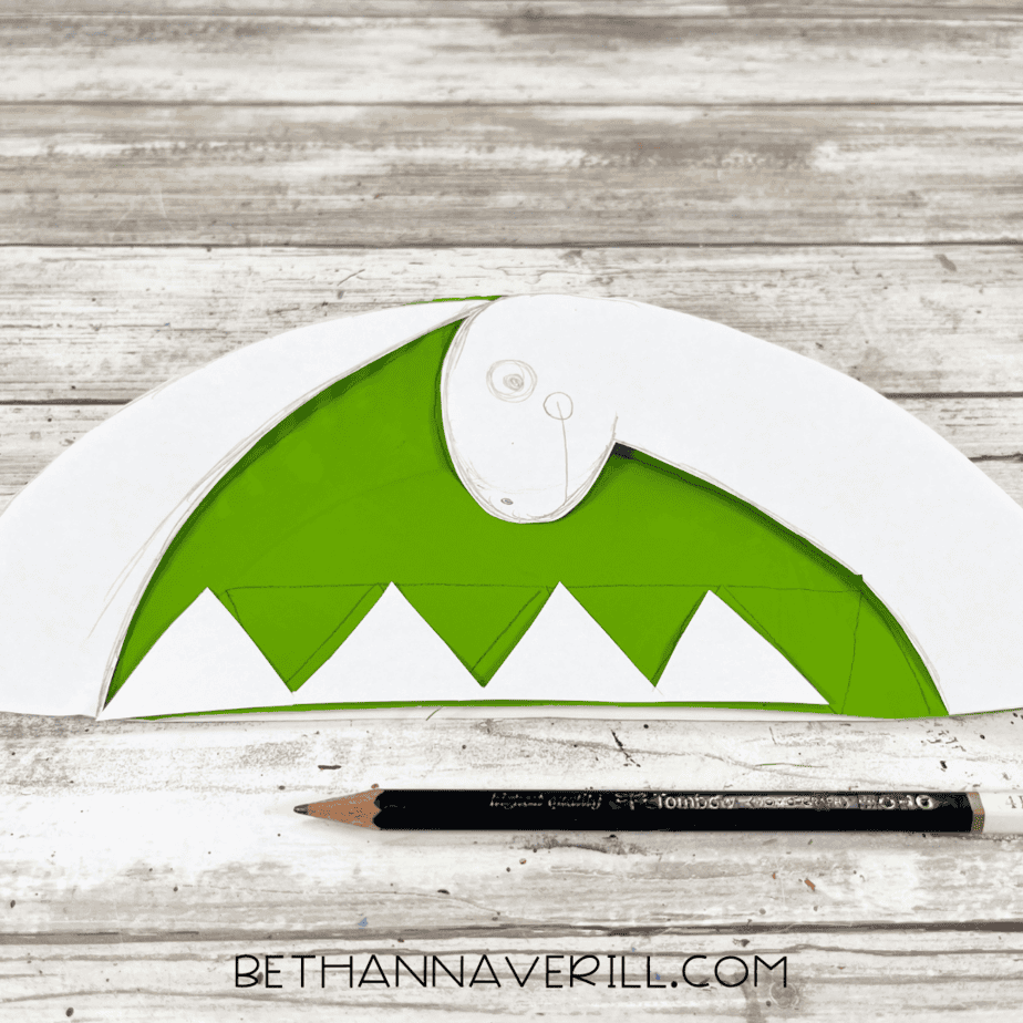 Pencil sketch of dinosaur shape on painted paper plate.