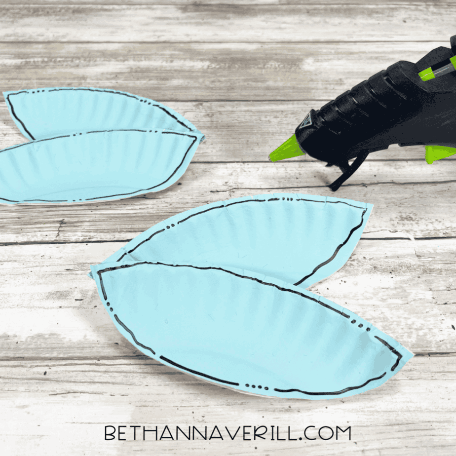 Blue paper plate wings glued together in pairs with a glue gun beside them.