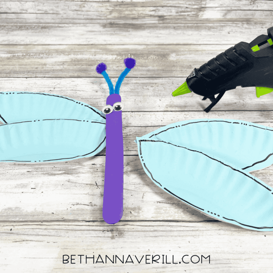 Purple dragonfly body with googly eyes and antennae placed next to blue wings.