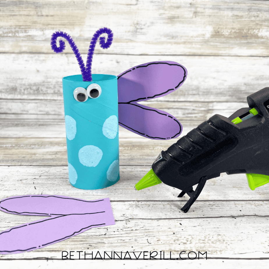 Dragonfly craft assembled with painted roll, googly eyes, pipe cleaner antennae, and one wing glued on.