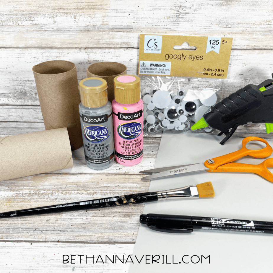 Materials for elephant paper roll craft including paint, googly eyes, scissors, glue, and toilet paper rolls.