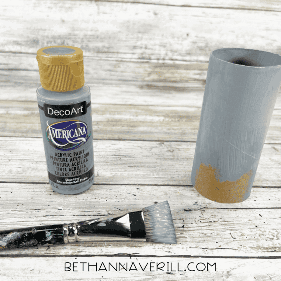Toilet paper roll painted gray with paintbrush and paint bottle beside it.